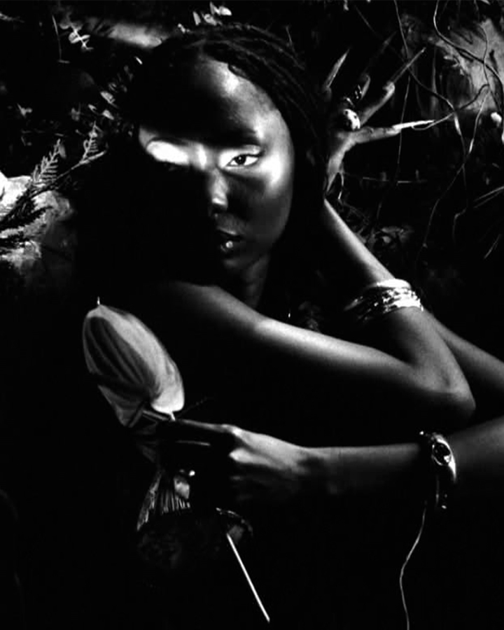 Black and white shot of a model with deep skin holding a flower with a beam of light cascading over her eyes.